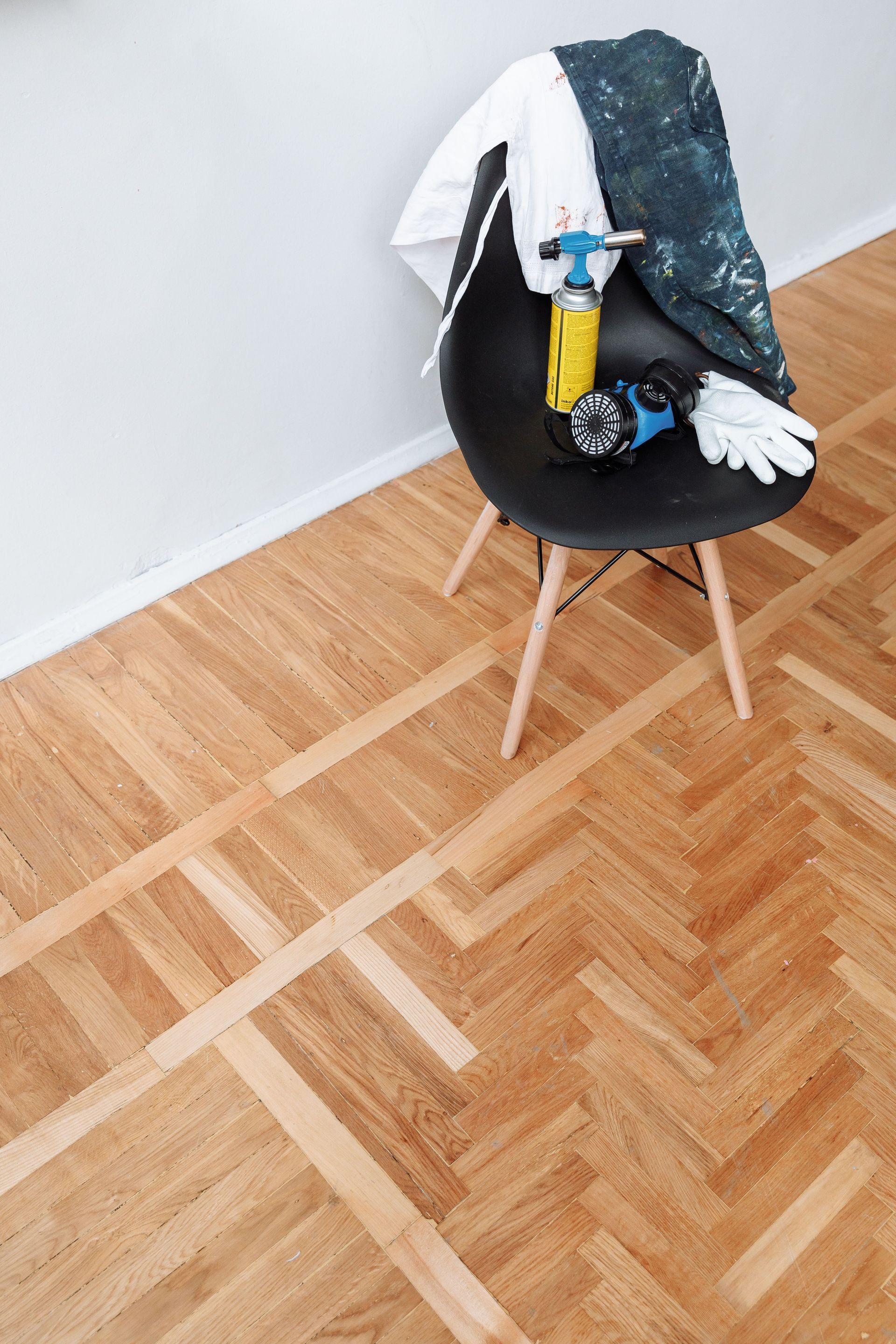 Woodworking tools on chair with parquet floor surface, featuring a blowtorch, gloves, and protective gear.